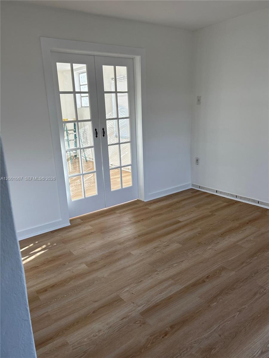 A room with light wood-look flooring and white walls features a set of French doors — MIAMI, FL