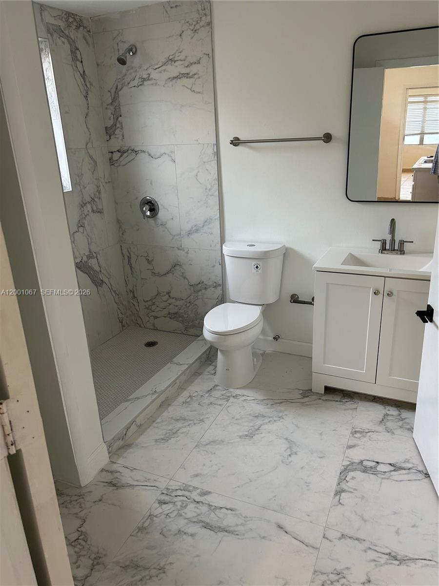 A bathroom features a marble-tiled shower, a white vanity, and matching marble floor tiles — MIAMI, FL