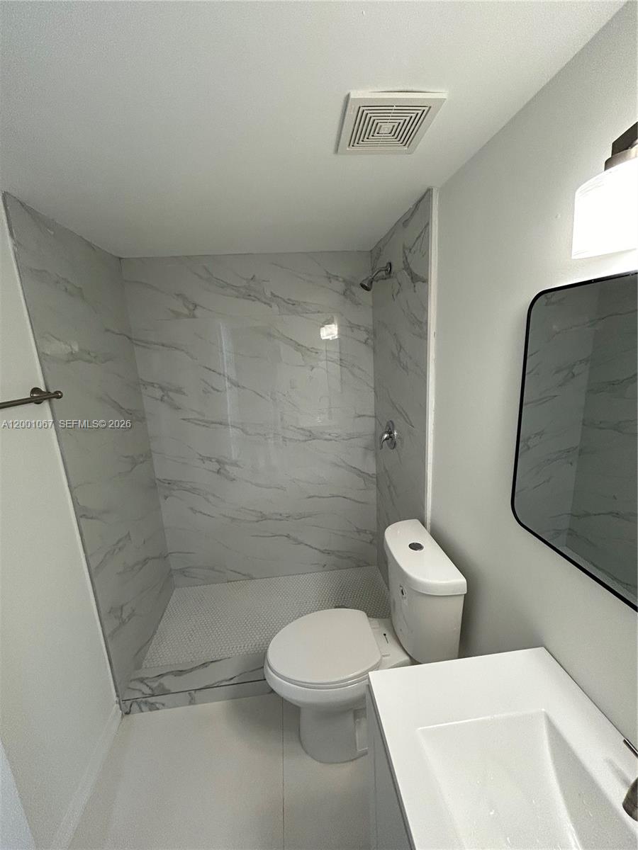 A bathroom features a walk-in shower with marble-patterned tile, a white toilet, and a vanity — MIAMI, FL