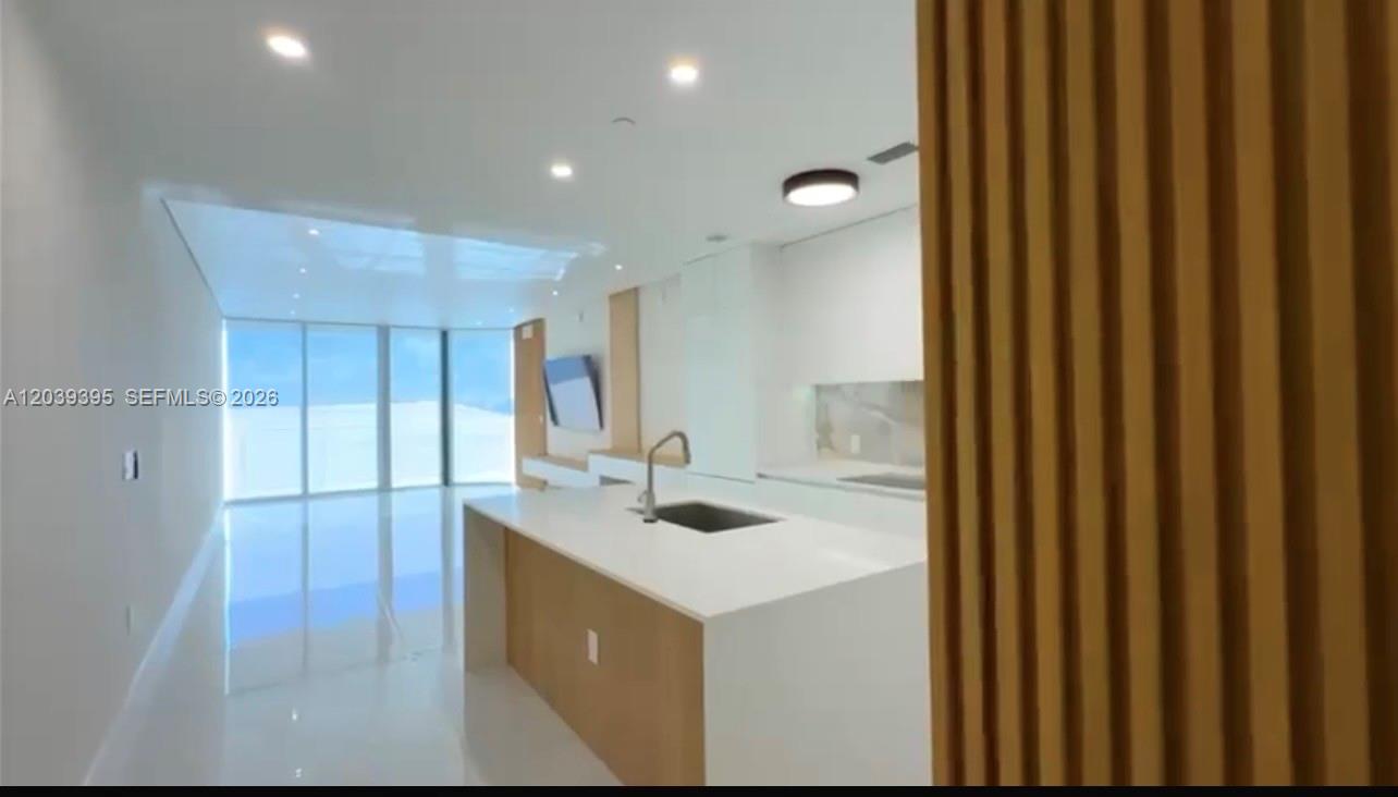 A modern kitchen with a white island and light wood accents overlooks a bright living area — 700 NE 24th St # 1505, Miami FL 33137, MIAMI, FL