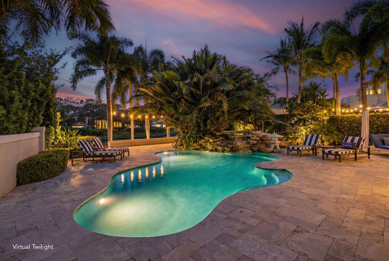 A backyard swimming pool with a stone waterfall, lounge chairs, and palm trees at twilight — 116 Terrapin Trail, Jupiter FL 33458, JUPITER, FL