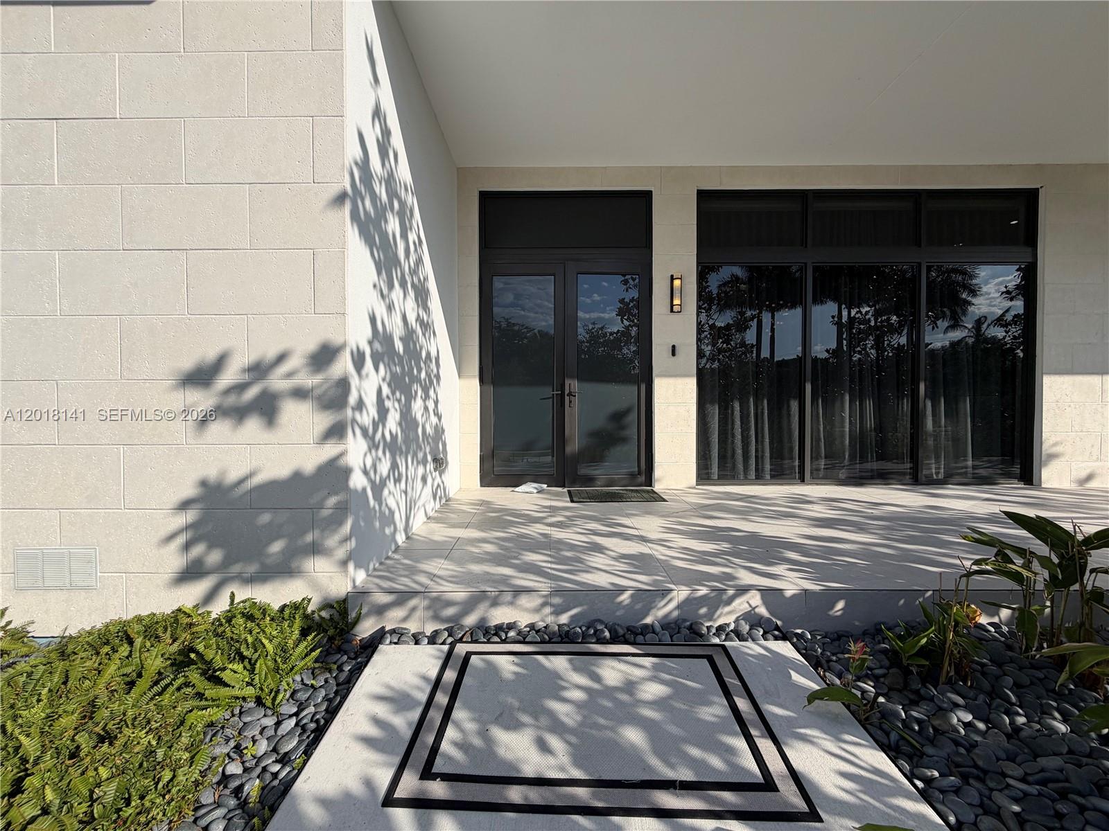 A modern home entrance features a glass double door, large light-colored tiles, and stone landscaping — 16786 Natures Way, Weston FL 33326, WESTON, FL