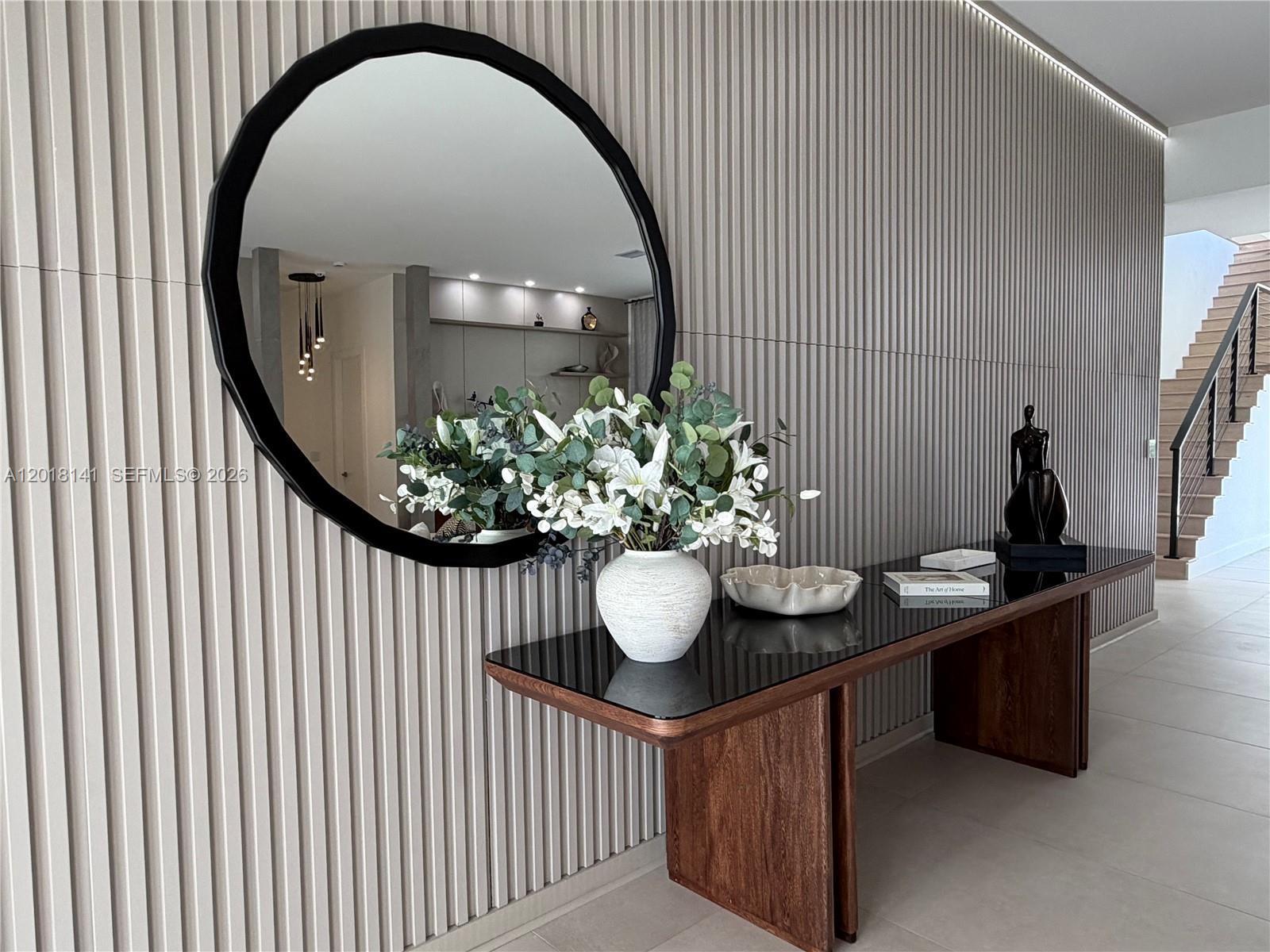 A modern entryway features a round black mirror, a glass-topped console table, and slatted wall paneling — 16786 Natures Way, Weston FL 33326, WESTON, FL