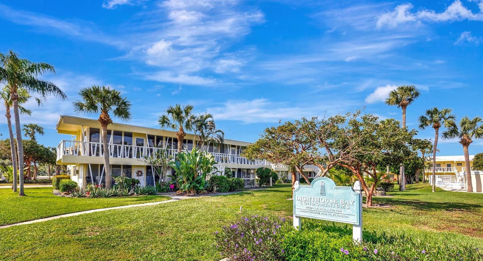 A two-story condominium building with palm trees and a sign on a grassy lawn — 2755 NE 28th Avenue # A3, Lighthouse Point FL 33064, LIGHTHOUSE POINT, FL