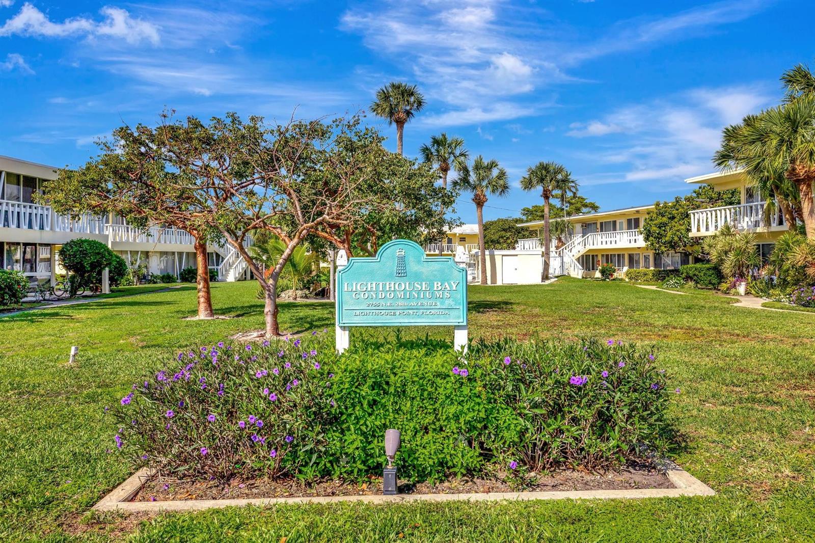 A sign for Lighthouse Bay Condominiums stands in a grassy courtyard between two residential buildings — 2755 NE 28th Avenue # A3, Lighthouse Point FL 33064, LIGHTHOUSE POINT, FL