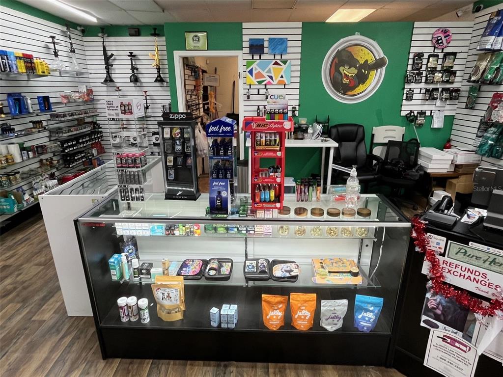 A retail shop interior features glass display cases, wall-mounted shelving, and green-painted walls — 5915 MEMORIAL HIGHWAY, TAMPA, FL