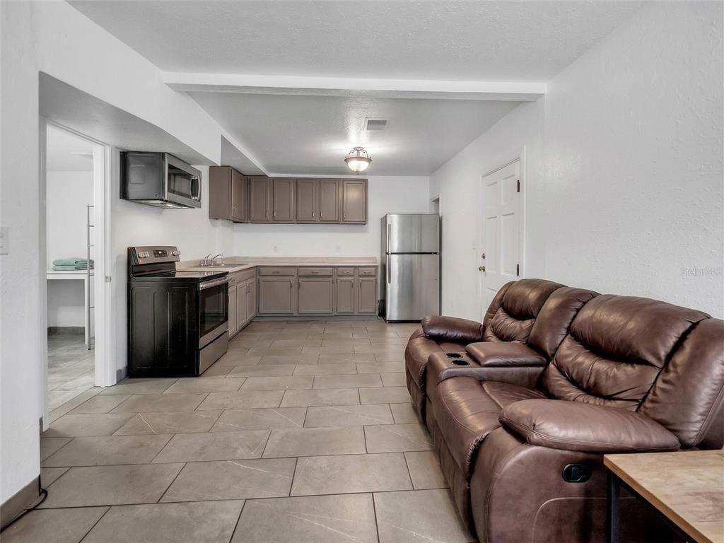 An open-concept kitchen and living area features tile flooring, brown cabinetry, and a leather sofa — 2600 EUSTON ROAD, WINTER PARK, FL