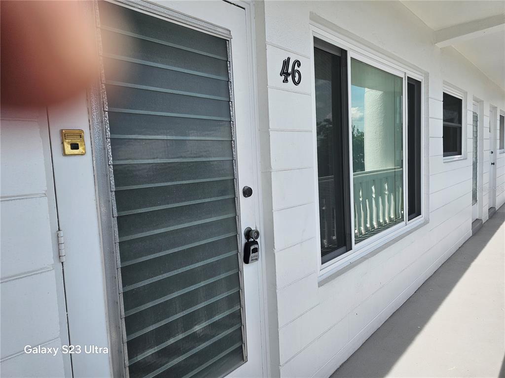 A white exterior door with a louvered storm door and a window labeled 46 — 2454 AUSTRALIA WAY E UNIT 46, CLEARWATER, FL
