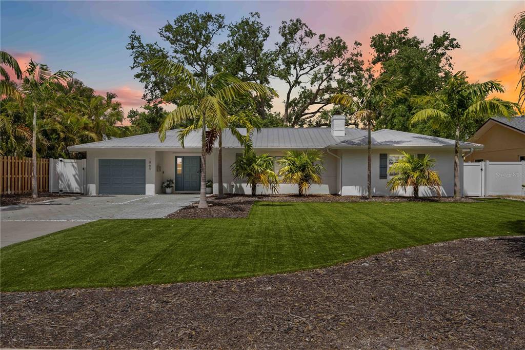 A single-story house with a metal roof, gray garage, and palm trees on a lawn — 1865 ORCHID STREET, SARASOTA, FL