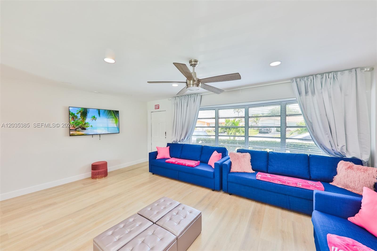 A living room features blue sofas, a wall-mounted television, and light wood flooring — HOLLYWOOD, FL