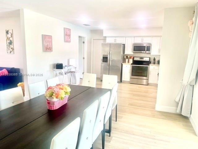 A dining area with a dark wood table leads into a modern kitchen with stainless appliances — HOLLYWOOD, FL