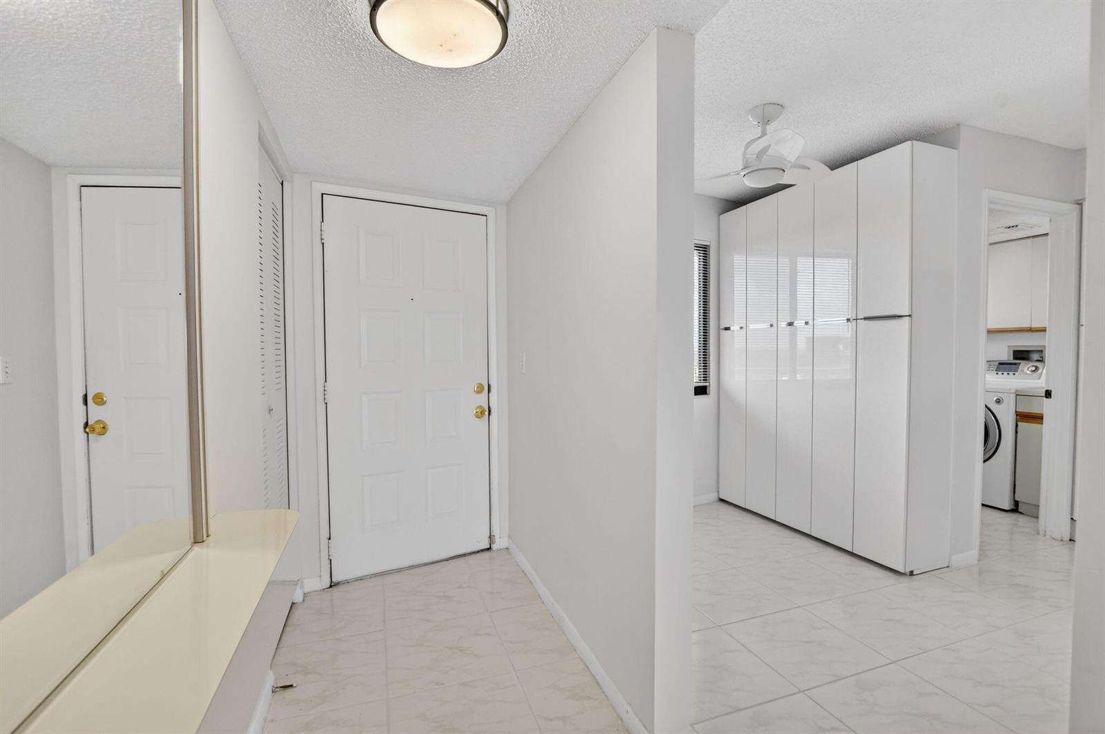 A bright entryway features white tile floors, a white front door, and built-in storage cabinets — 7370 S Oriole Boulevard # 802, Delray Beach FL 33446, DELRAY BEACH, FL