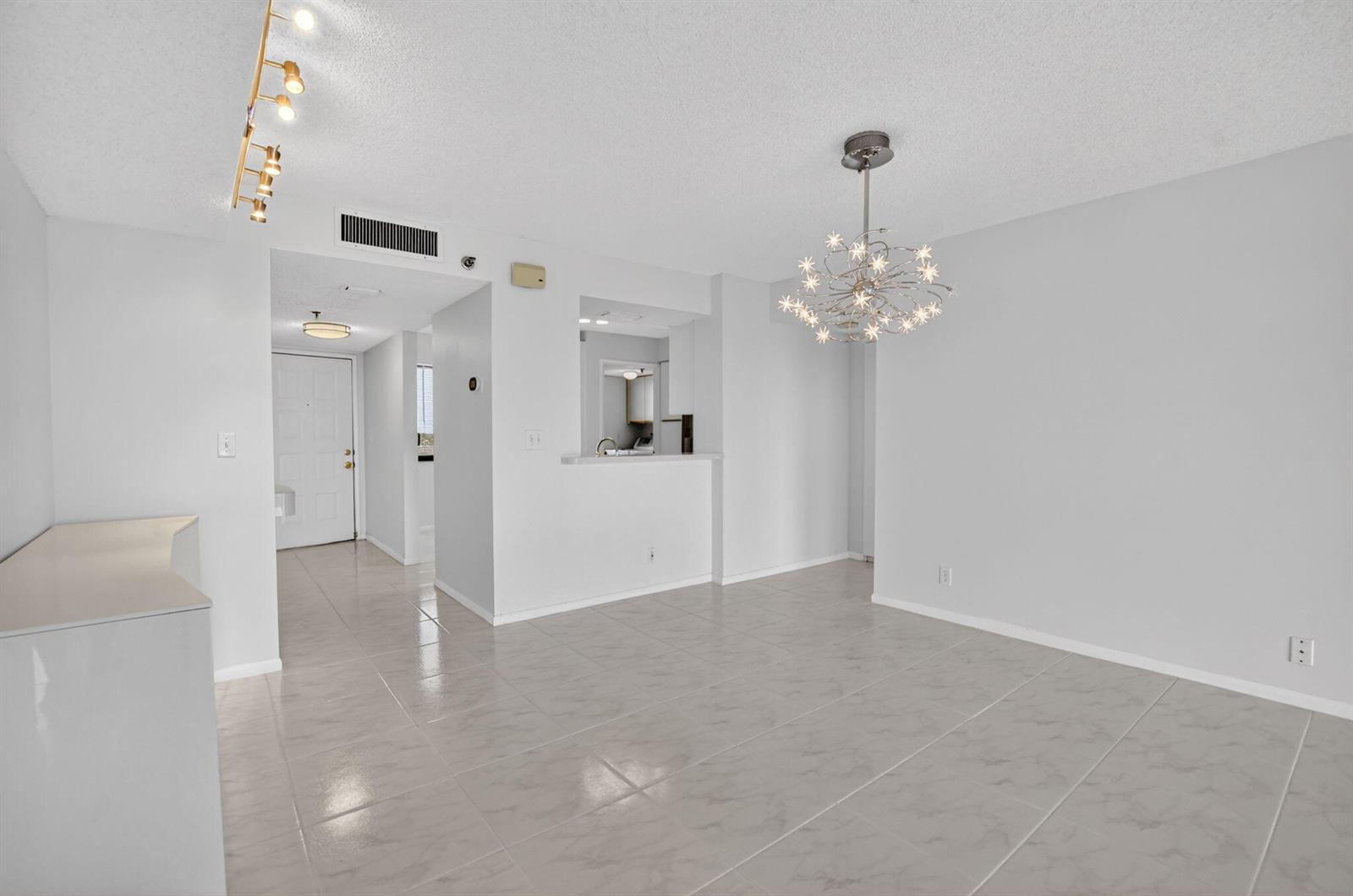 An open-concept dining area features light gray tile flooring, a starburst chandelier, and track lighting — 7370 S Oriole Boulevard # 802, Delray Beach FL 33446, DELRAY BEACH, FL
