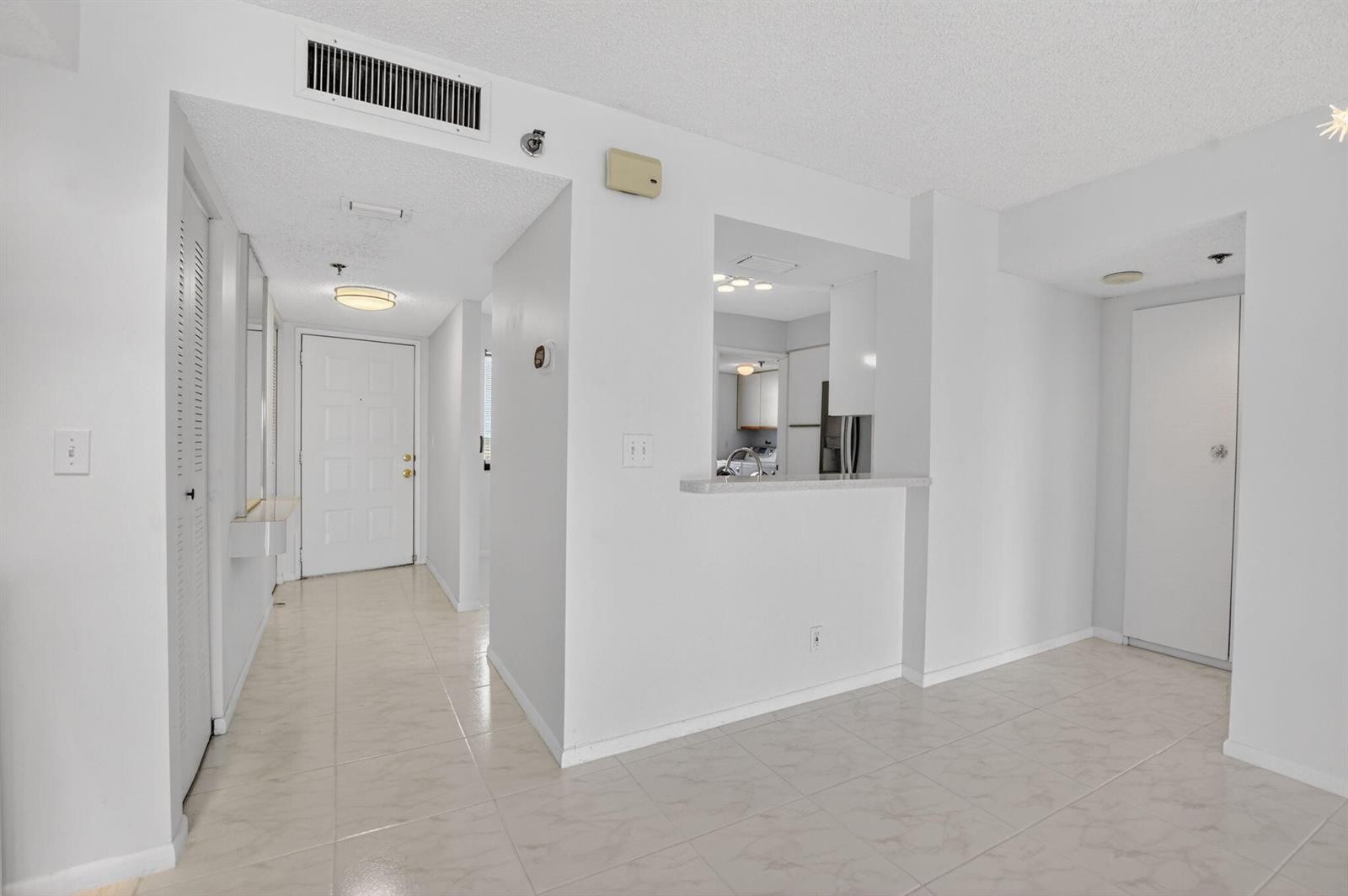 An interior view showing a tiled entryway, a kitchen pass-through window, and a white door — 7370 S Oriole Boulevard # 802, Delray Beach FL 33446, DELRAY BEACH, FL