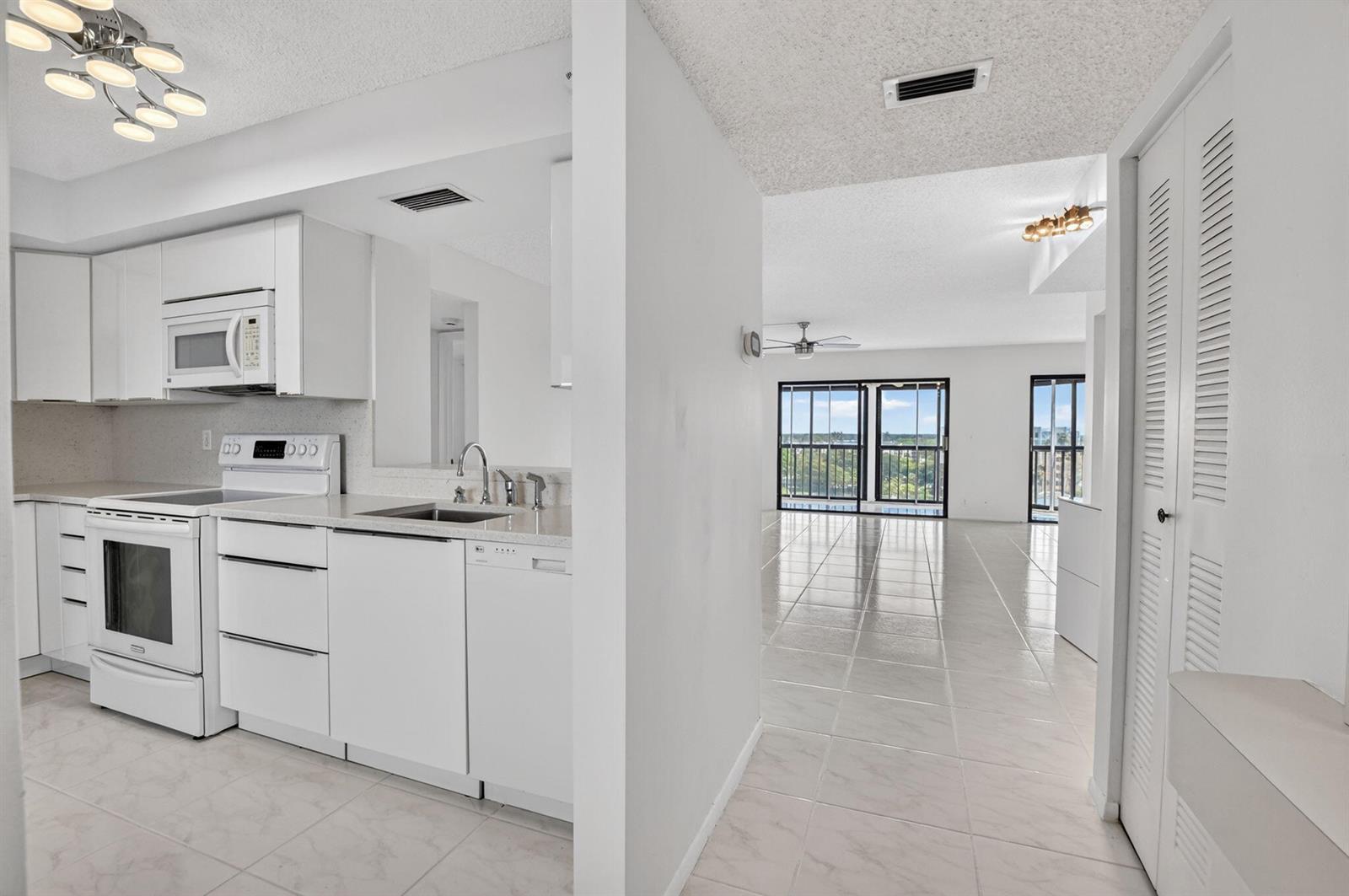 A white kitchen with tile floors opens into a bright living area with balcony views — 7370 S Oriole Boulevard # 802, Delray Beach FL 33446, DELRAY BEACH, FL