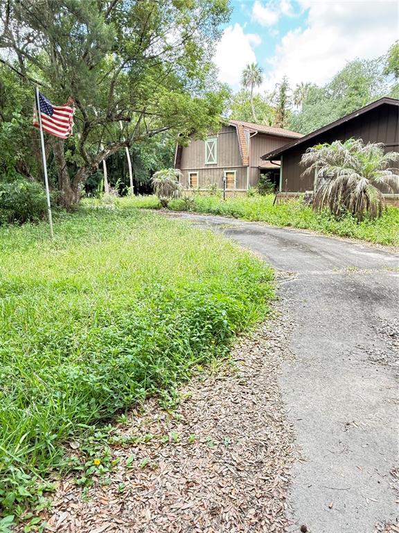 A paved driveway leads toward a two-story barn-style house surrounded by trees and overgrown grass — 2260 HONTOON ROAD, DELAND, FL