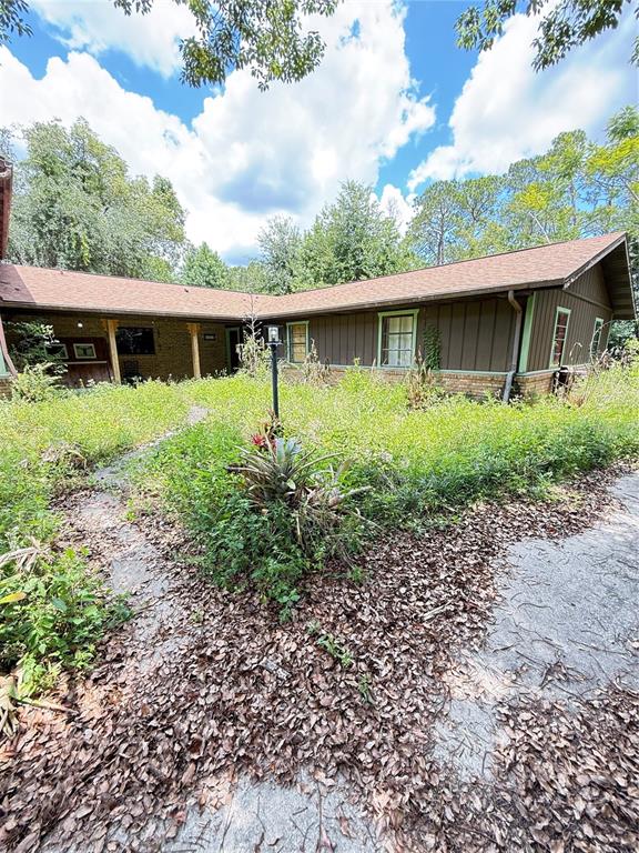 An exterior view of a brown house with a large, overgrown yard and leaf-covered walkway — 2260 HONTOON ROAD, DELAND, FL