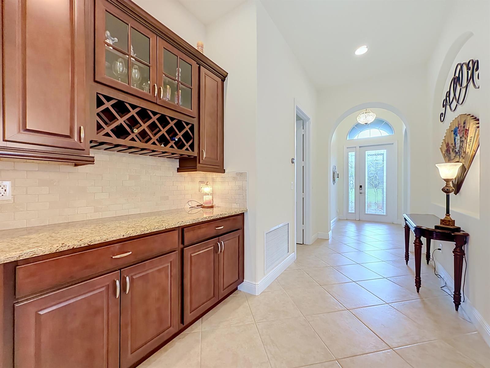 A hallway features a built-in wet bar with dark wood cabinets and a granite countertop — 728 Fortunella Circle SW, Vero Beach FL 32968, VERO BEACH, FL