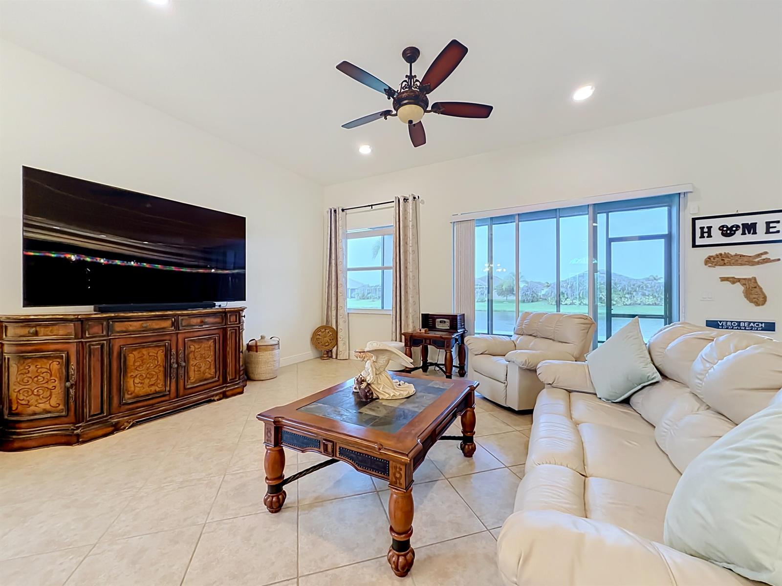 A living room features a large television, wooden furniture, a white sofa, and sliding doors — 728 Fortunella Circle SW, Vero Beach FL 32968, VERO BEACH, FL