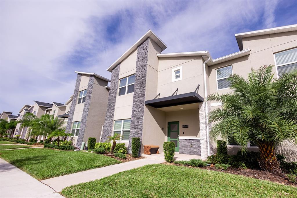 A multi-story townhouse exterior features tan stucco walls, stone veneer accents, and a green front door — 8967 CABOT CLIFFS DRIVE, KISSIMMEE, FL