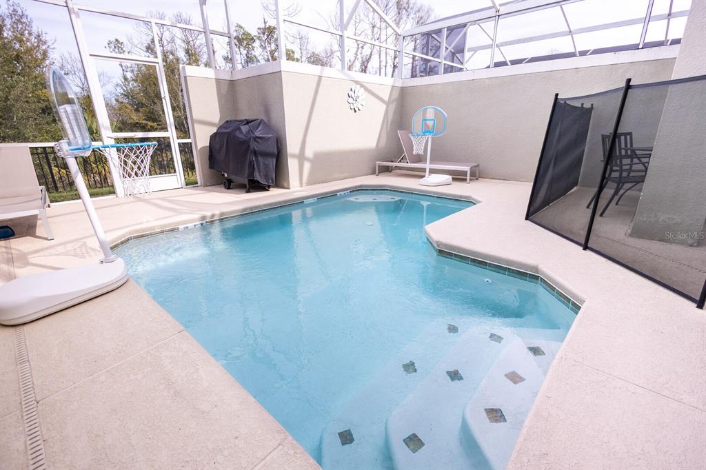 A screened-in patio features a small swimming pool with steps and a basketball hoop — 8967 CABOT CLIFFS DRIVE, KISSIMMEE, FL