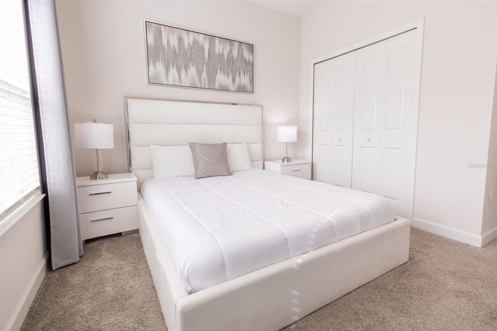 A bedroom features a white upholstered bed, two nightstands with lamps, and a closet — 8967 CABOT CLIFFS DRIVE, KISSIMMEE, FL