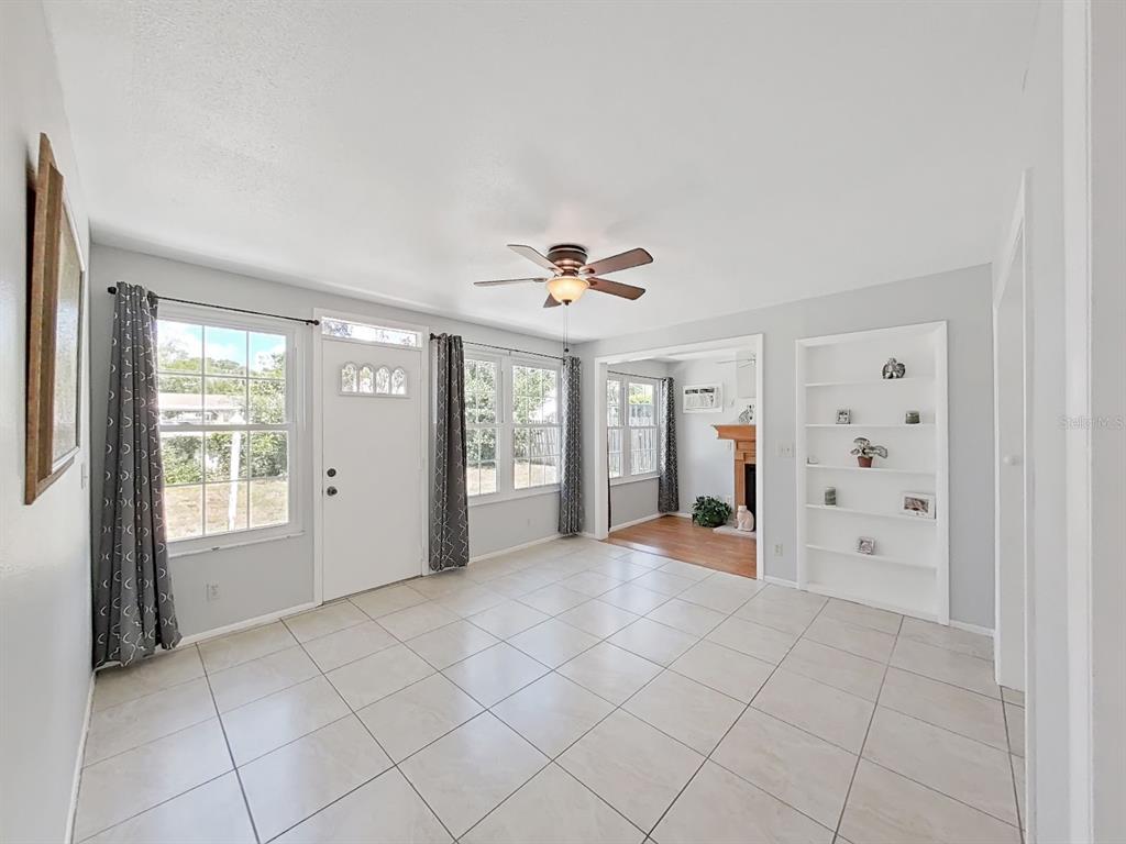A bright living room features light tile flooring, a ceiling fan, and built-in wall shelving — 878 RUSTIC OAKS DRIVE, PALM HARBOR, FL