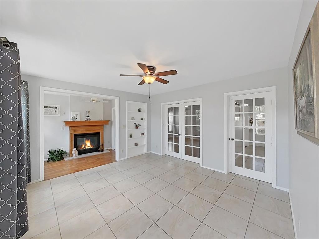 A living room with tile flooring, a fireplace, built-in shelving, and French doors — 878 RUSTIC OAKS DRIVE, PALM HARBOR, FL
