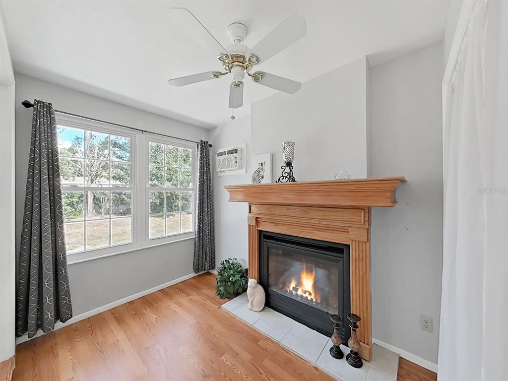 A living room features a fireplace with a wooden mantel, hardwood floors, and a ceiling fan — 878 RUSTIC OAKS DRIVE, PALM HARBOR, FL