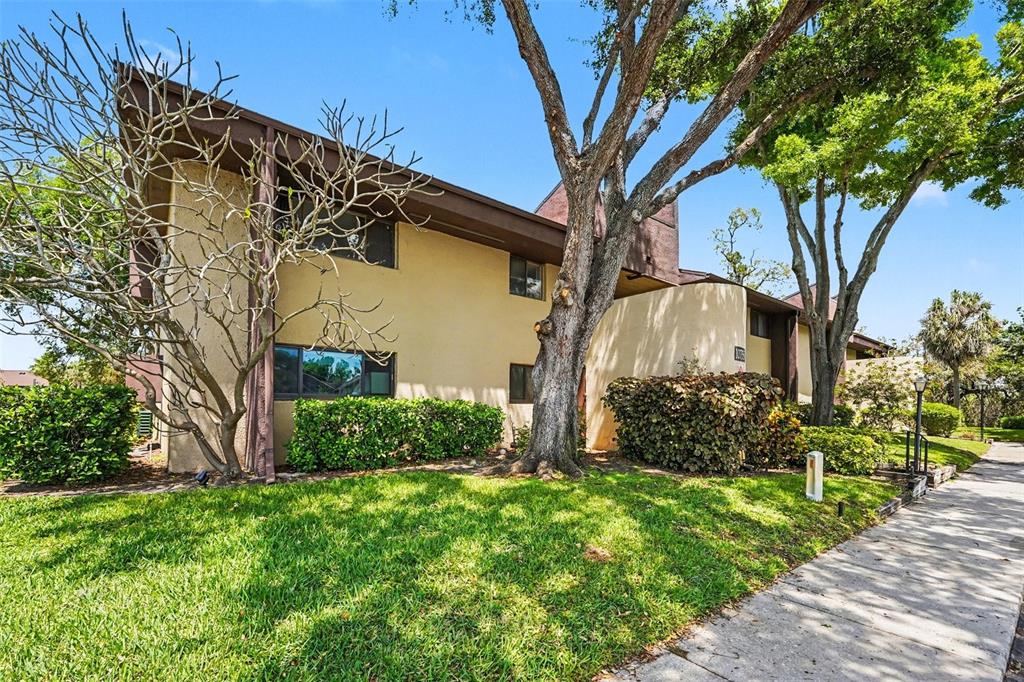 A two-story tan building with brown trim is surrounded by trees and green landscaping — 10755 VILLAGE CLUB CIRCLE N UNIT 101, ST PETERSBURG, FL