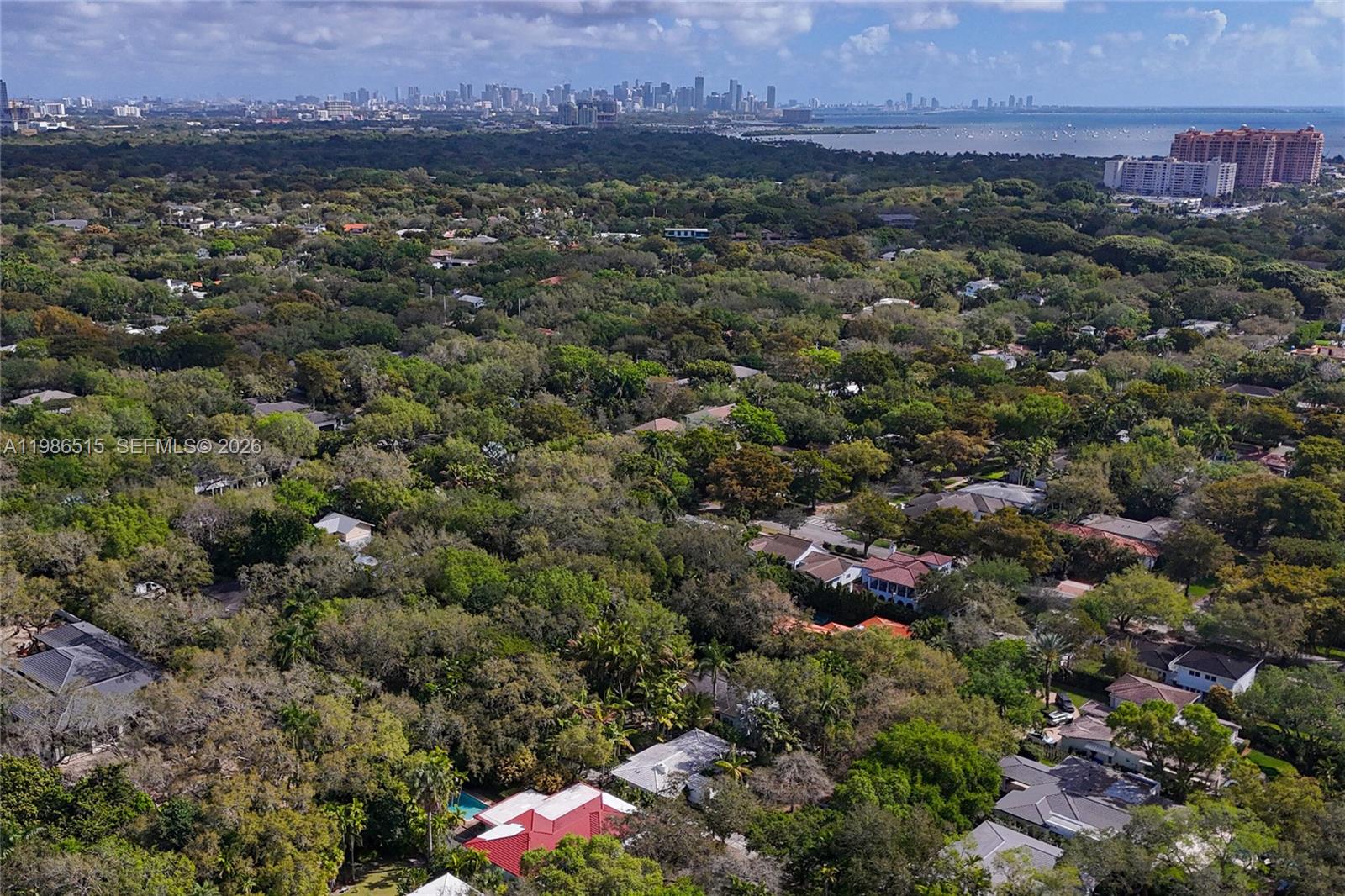 An aerial view shows a dense, tree-filled residential neighborhood with a distant city skyline — 731 San Juan Dr, Coral Gables FL 33143, CORAL GABLES, FL