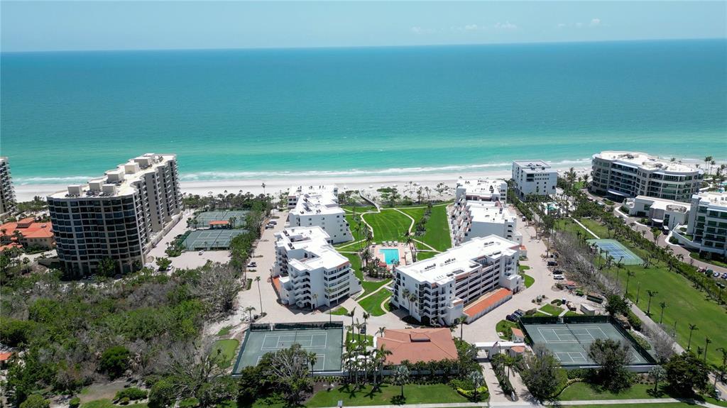 An aerial view shows a coastal resort complex with multiple buildings, swimming pools, and tennis courts — 1425 GULF OF MEXICO DRIVE UNIT 408, LONGBOAT KEY, FL