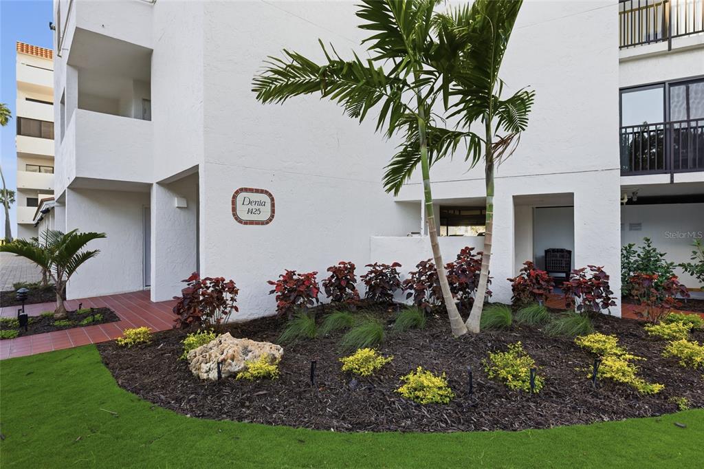 A white multi-story building exterior features a landscaped garden bed with palm trees and shrubs — 1425 GULF OF MEXICO DRIVE UNIT 408, LONGBOAT KEY, FL