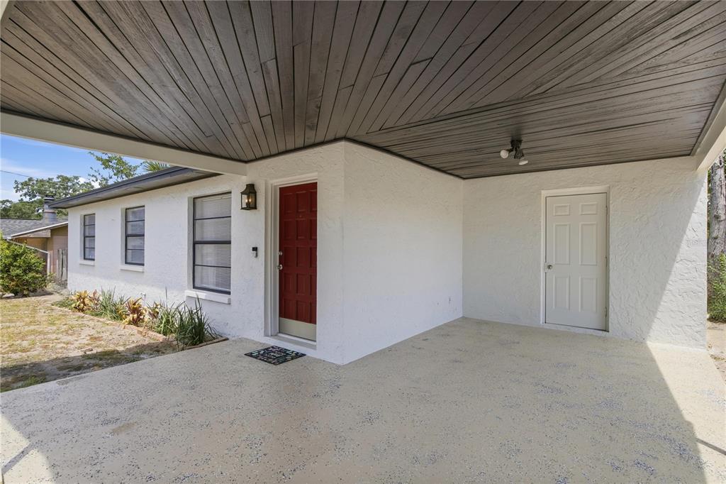 A covered concrete porch features a red front door and a white side door — 4606 E LINEBAUGH AVENUE, TAMPA, FL