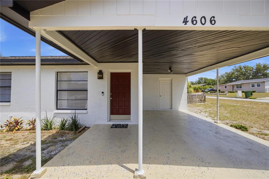 A white house exterior features a red front door and a covered concrete carport — 4606 E LINEBAUGH AVENUE, TAMPA, FL