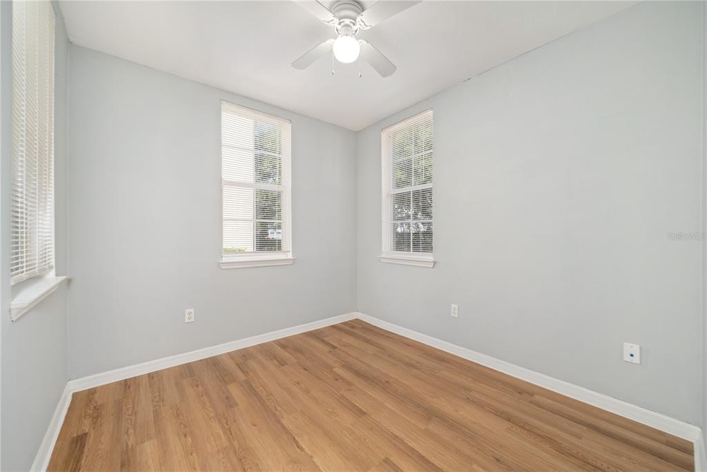 An empty room features light blue walls, wood-look flooring, two windows, and a ceiling fan — 714 SIENA PALM DRIVE UNIT 104, CELEBRATION, FL