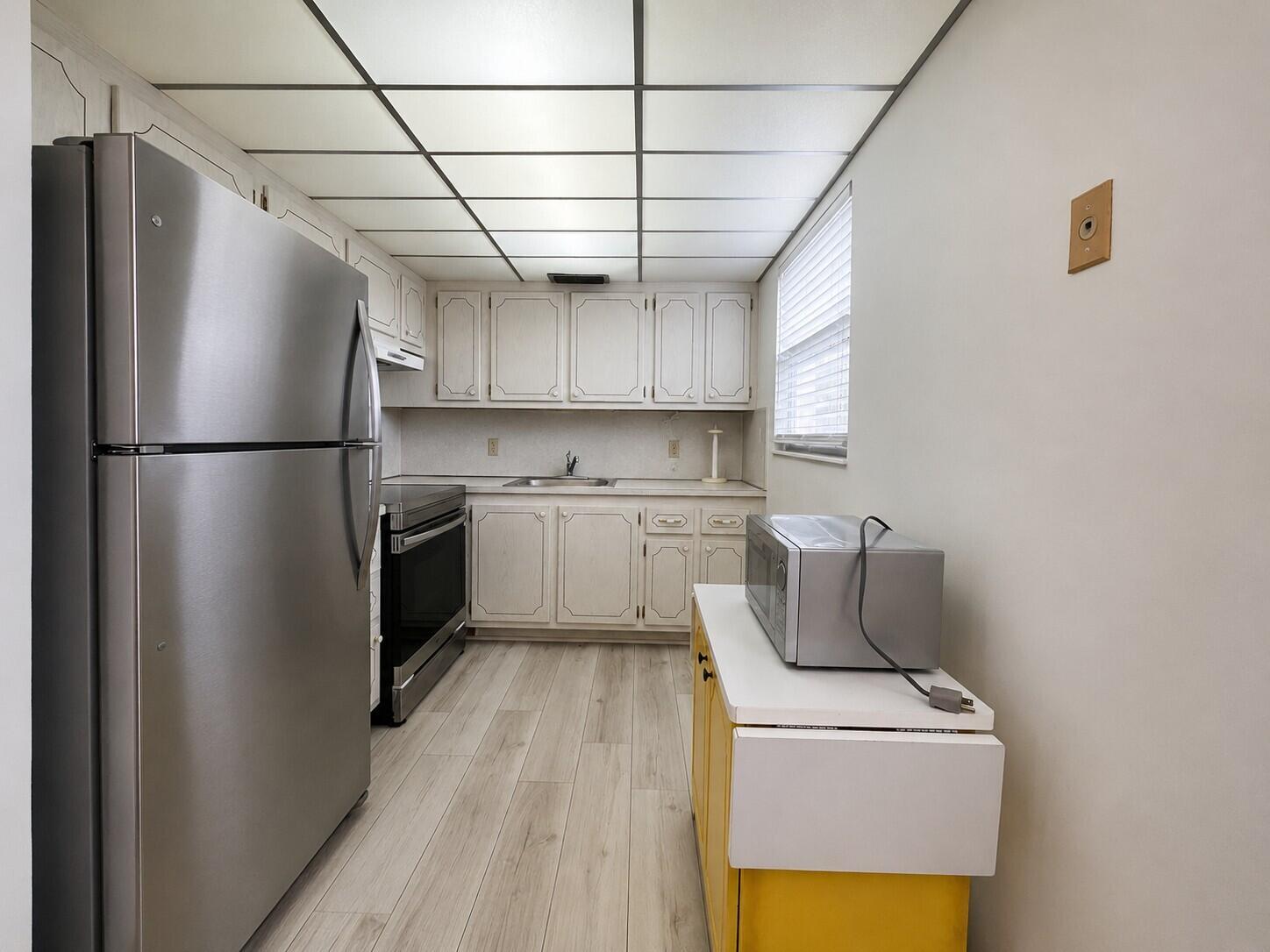 A kitchen features stainless steel appliances, white cabinetry, light wood flooring, and a drop-ceiling grid — 333 Farnham P, Deerfield Beach FL 33442, DEERFIELD BEACH, FL