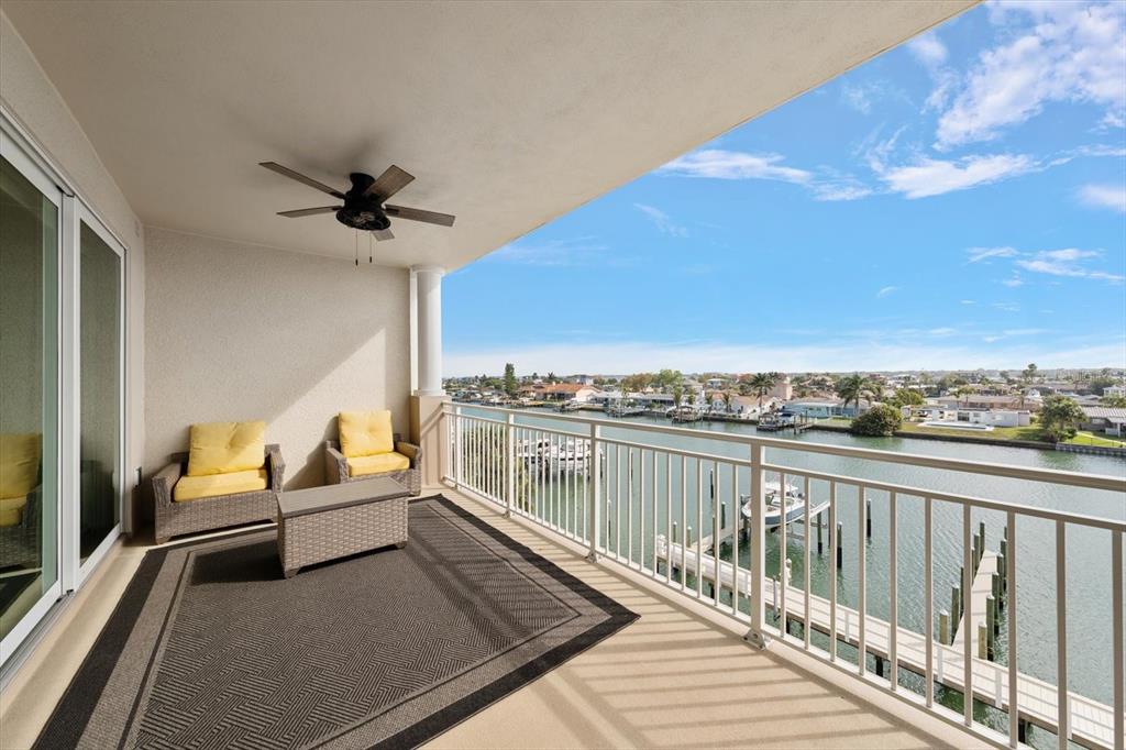 A covered balcony features wicker chairs, a ceiling fan, and a view of the water — 125 ISLAND WAY UNIT 402, CLEARWATER BEACH, FL