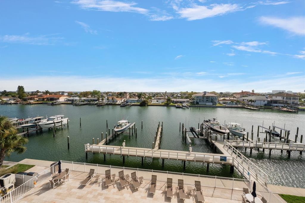 An elevated view of a waterfront patio with lounge chairs overlooking a boat dock — 125 ISLAND WAY UNIT 402, CLEARWATER BEACH, FL