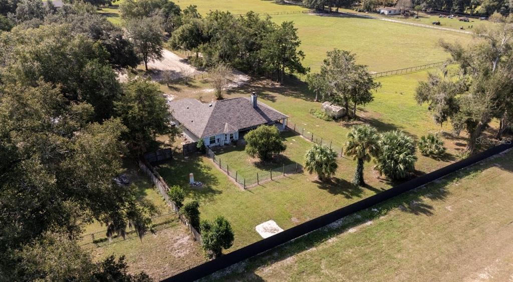An aerial view shows a house with a gray roof surrounded by trees and fenced yards — 1801 NE 77TH STREET, OCALA, FL