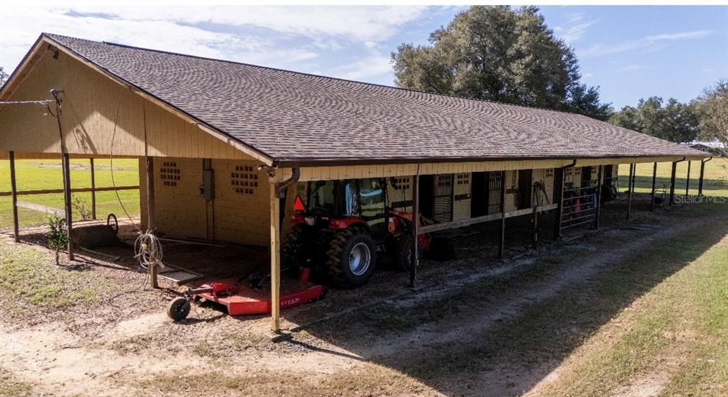 A long, open-sided barn with a shingled roof houses a red tractor and farm equipment — 1801 NE 77TH STREET, OCALA, FL
