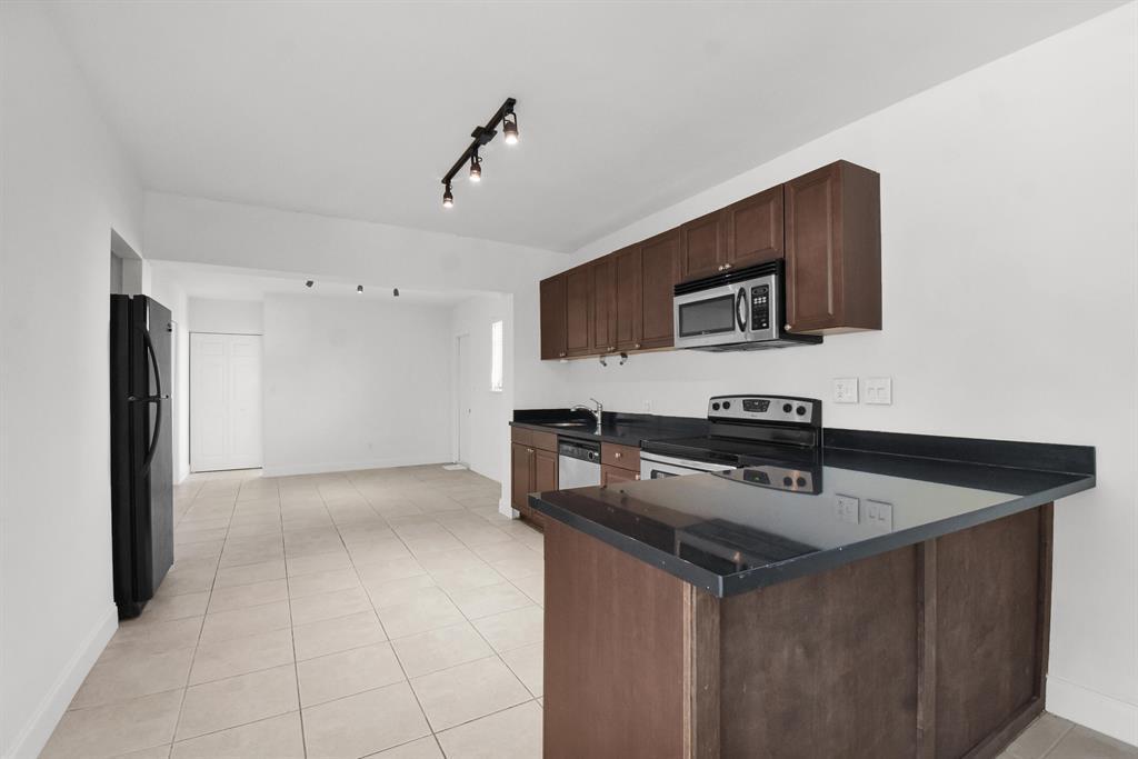 A kitchen with dark wood cabinets, black countertops, and tile flooring opens to a living area — 1116 S 17th Avenue S, Hollywood FL 33020, HOLLYWOOD, FL