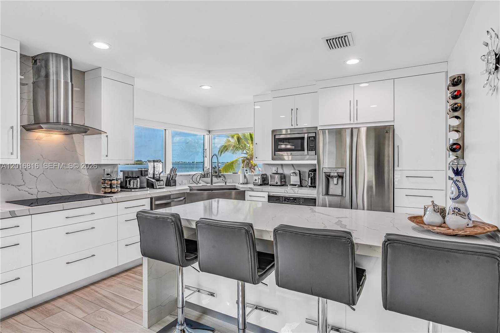 A modern kitchen features white cabinetry, marble countertops, stainless steel appliances, and a breakfast bar — 325 Calusa, Key Largo FL 33037, KEY LARGO, FL