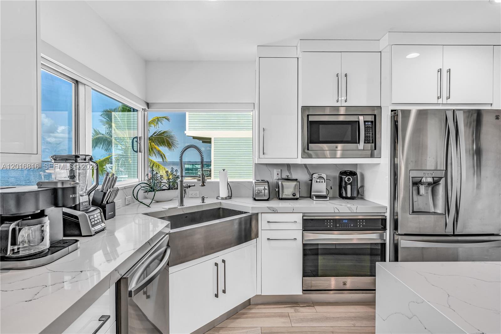 A modern white kitchen features a stainless steel farmhouse sink, marble countertops, and ocean views — 325 Calusa, Key Largo FL 33037, KEY LARGO, FL