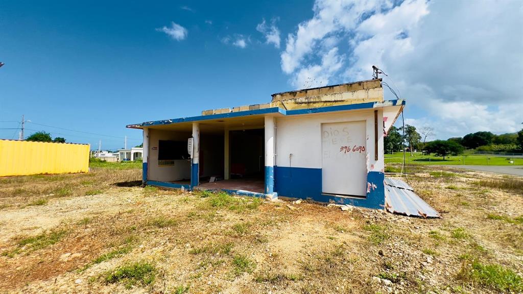 A weathered, single-story concrete building with blue trim stands on a dry, grassy lot — km 5.1 CARRETERA 467, AGUADILLA, PR