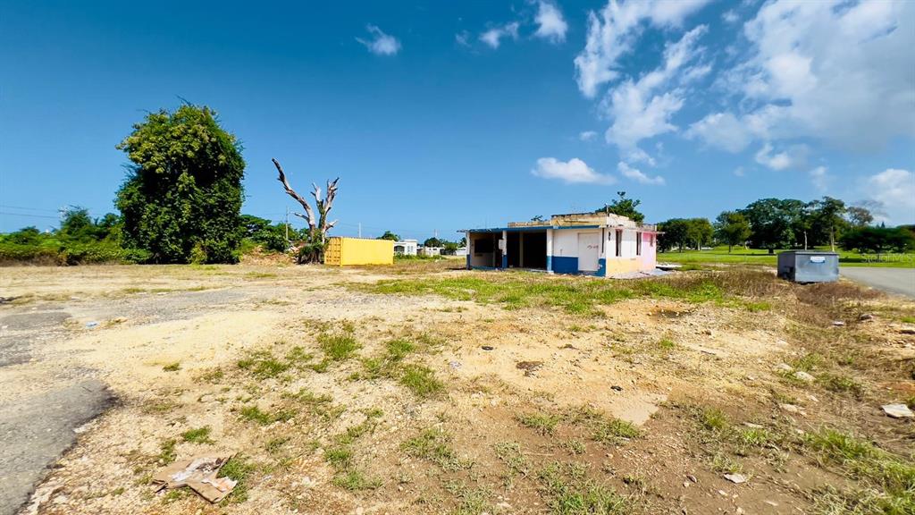 A dilapidated, single-story building sits on a large, unpaved lot under a blue sky — km 5.1 CARRETERA 467, AGUADILLA, PR