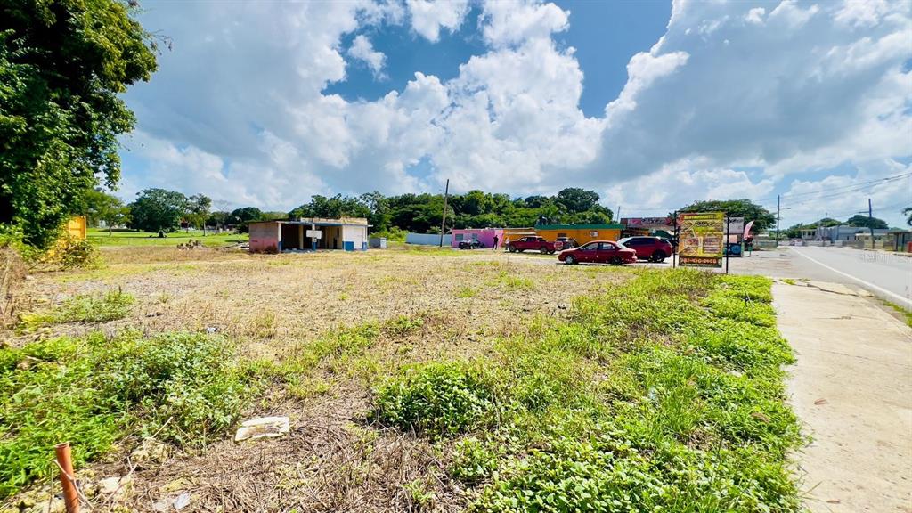 A vacant, grassy lot sits next to a small building and a paved road — km 5.1 CARRETERA 467, AGUADILLA, PR