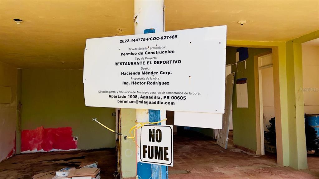 A construction permit sign hangs in an unfinished room with green walls and tile flooring — km 5.1 CARRETERA 467, AGUADILLA, PR