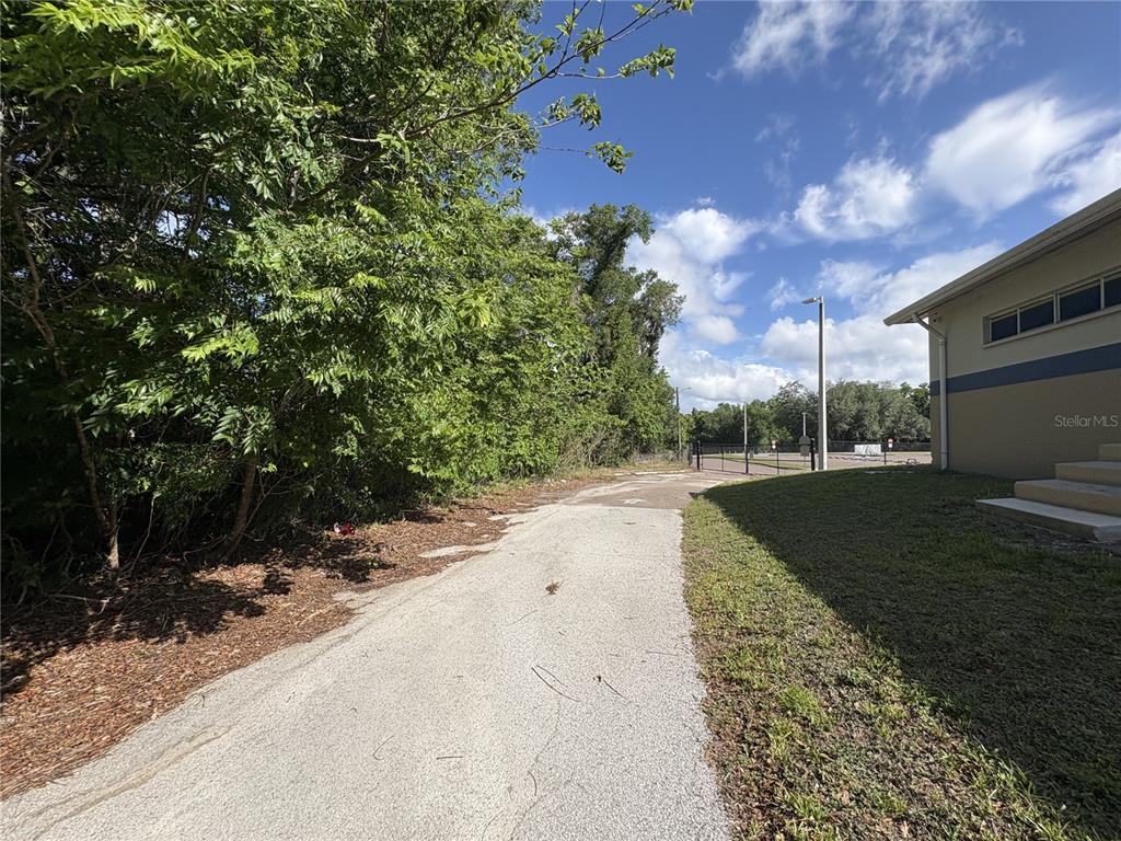 A paved path runs between a building and a wooded area toward a gated entrance — 14527 13TH STREET, DADE CITY, FL