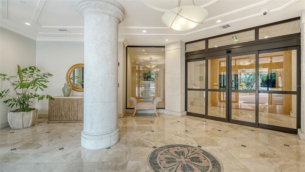 A bright lobby features marble floors, a large stone column, and glass sliding entrance doors — 1281 GULF OF MEXICO DRIVE UNIT 111, LONGBOAT KEY, FL